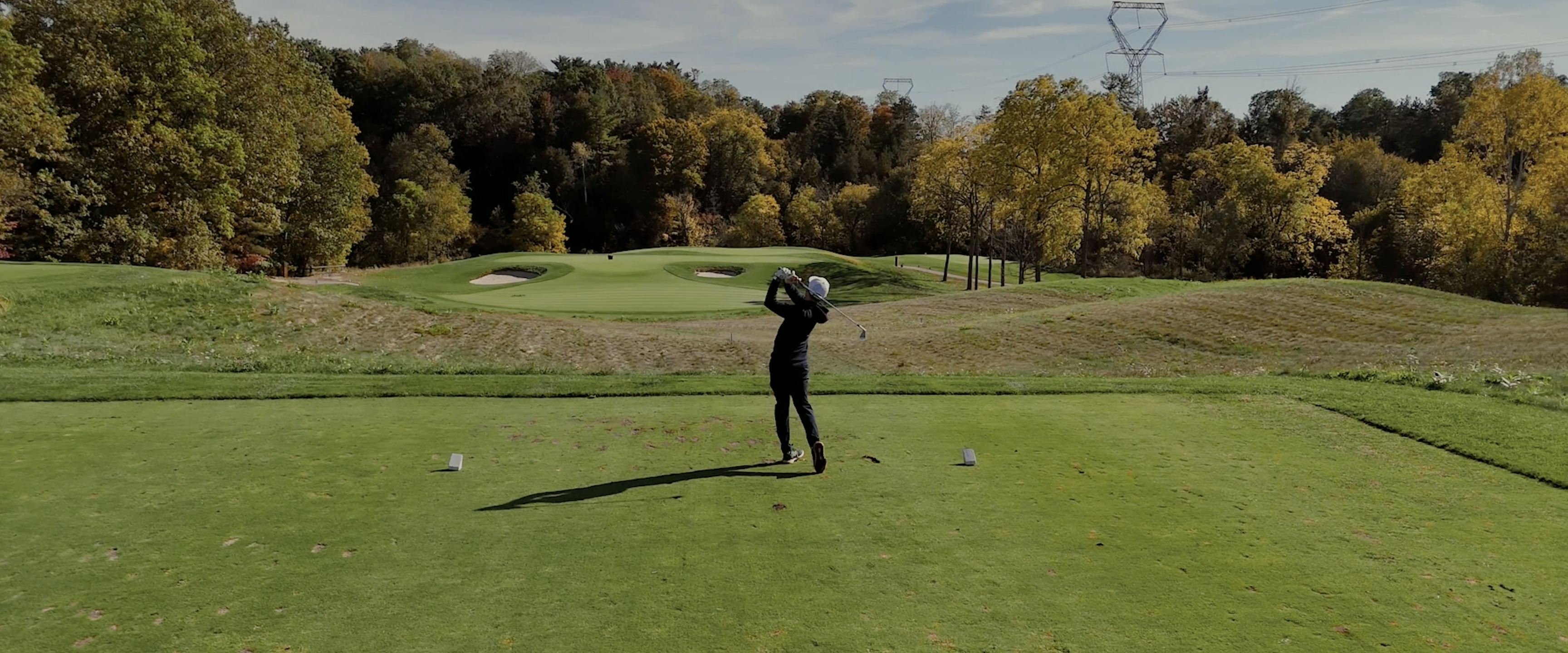 Golfer swinging on a wide green fairway with fall trees in the background